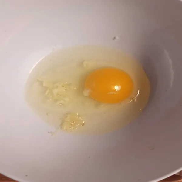 Tuang telur dalam mangkok, tambahkan bawang putih parut/ cincang, dan kocok lepas.