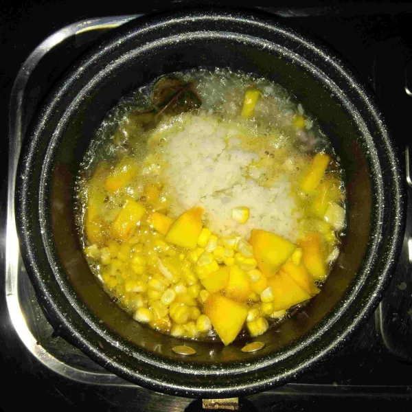 Masukkan nasi, labu kuning dan jagung manis ke dalam panci lalu aduk rata.