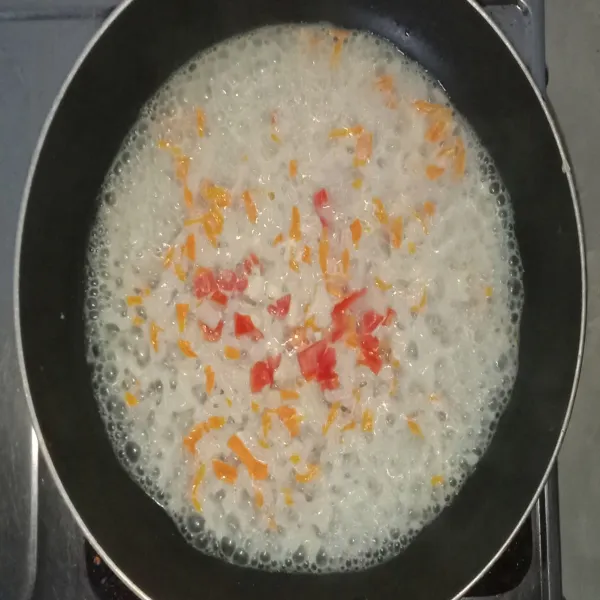 Tambahkan air dan nasi, aduk rata, lalu masukkan wortel aduk-aduk, dan masukkan juga tomat.
