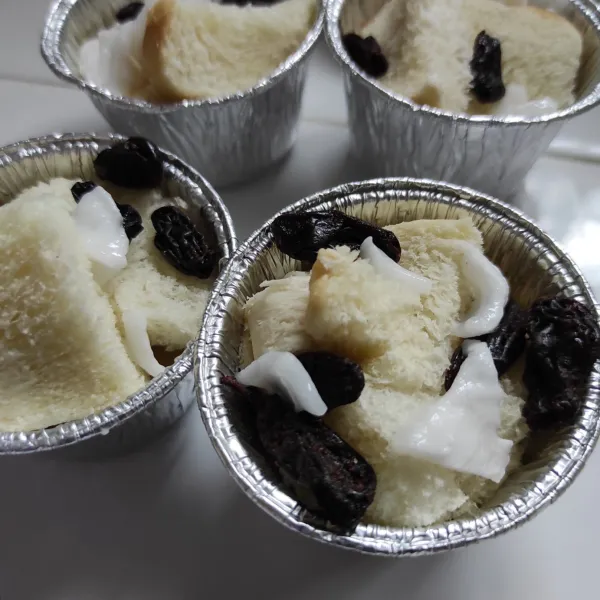 potong-potong roti, masukkan kedalam cup alumunium foil. tambahkan potongan buah kelapa dan kismis.