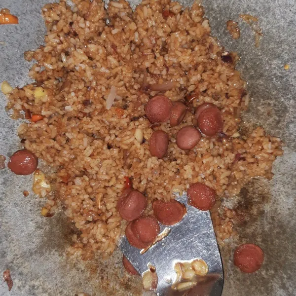 Masukkan nasi, masukkan kecap, aduk rata. Masukkan sosis, beri garam dan lada. Tes rasa. Sajikan dengan telur di atasnya.