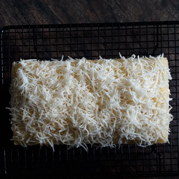 Setelah bolu sudah agak dingin keluarkan dari loyang. Olesi atasnya dengan margarin dan taburi keju cheddar parut.