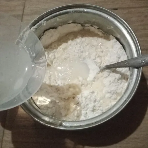 Tambahkan air sedikit demi sedikit sambil terus diaduk hingga semua bahan kering tercampur.