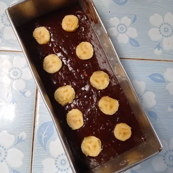 Masukkan adonan ke dalam loyang yang sudah dioles margarin dan dialas kertas roti. Tambahkan potongan pisang diatasnya.