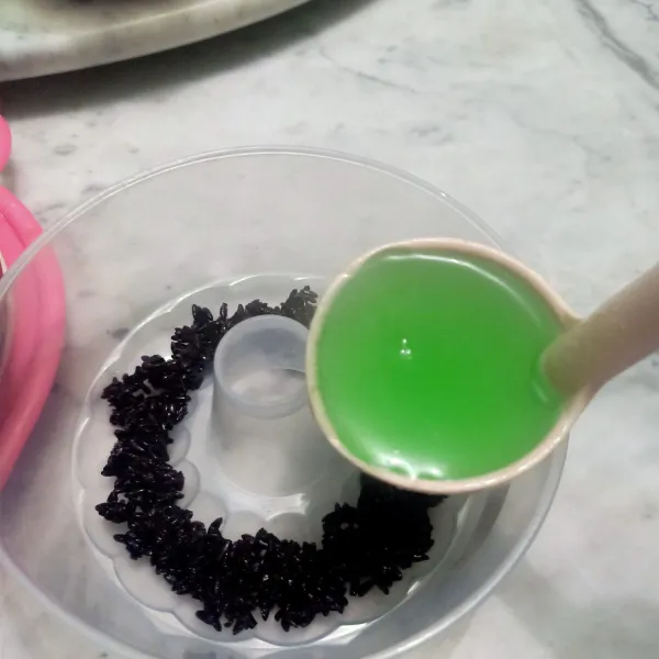 Siapkan wadah puding lalu taruh ketan hitam tape lalu sirami agar agar hijau perlahan. Jangan terlalu cepat dan pelan-pelan menuangkannya biar ketan hitam tape tidak berantakan.