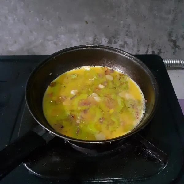 Sambil memasak, kocok telur ayam dengan kaldu bubuk. Kecilkan api dan tuang di wajan berisi tumisan pare yang sudah matang. Kemudian ratakan. Masak dengan api kecil.