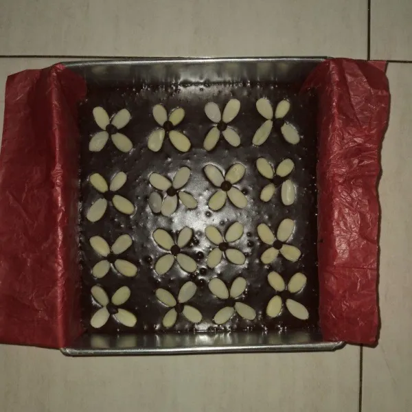 Panaskan oven, tuang adonan ke dalam loyang yang sudah di alasi baking paper, beri almond slice dan chocochips di atasnya, lalu diamkan adonan selama 10 menit.