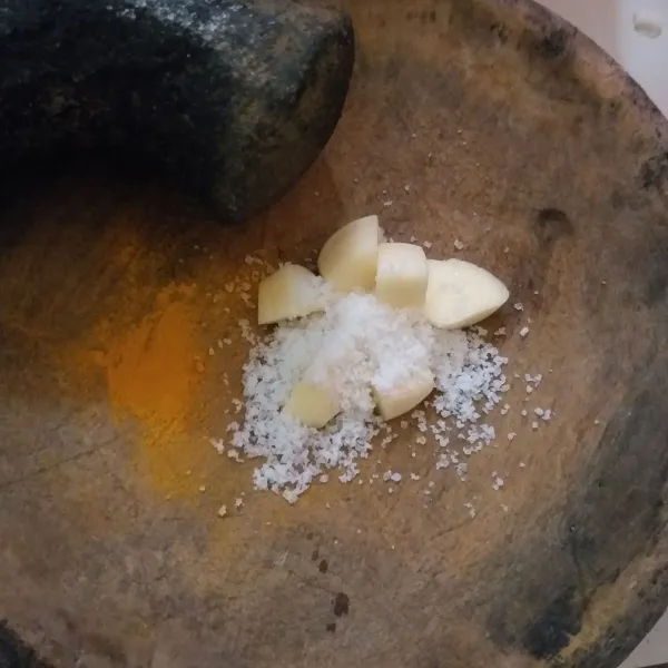 Haluskan bumbu, yang terdiri dari bawang putih, garam, dan kunyit bubuk.