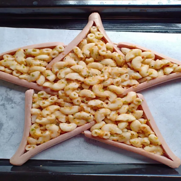 Belah sosis menjadi dua tanpa terputus, lalu bentuk sosis menjadi bintang dengan cara sematkan setiap bagian menggunakan lidi. Kemudian susun makaroni diantara sosis.