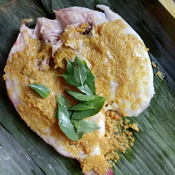 Siapkan daun pisang, beri bumbu lalu tata ikan diatasnya, beri bumbu di bagian dalam ikan, tambahkan daun kemangi