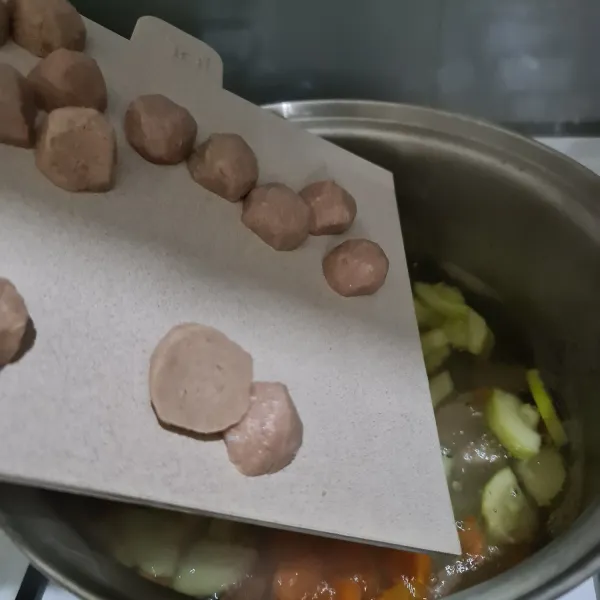 Potong bakso menjadi dua lalu masukkan ke dalam air rebusan.