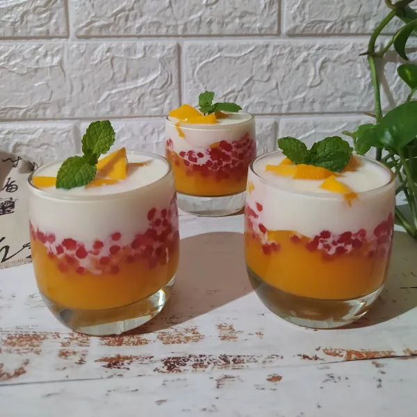 Tata di gelas, jus mangga, sagu mutiara, es batu lalu siram dengan susu UHT yang dicampur dengan krimer kental manis. Beri topping potongan mangga.