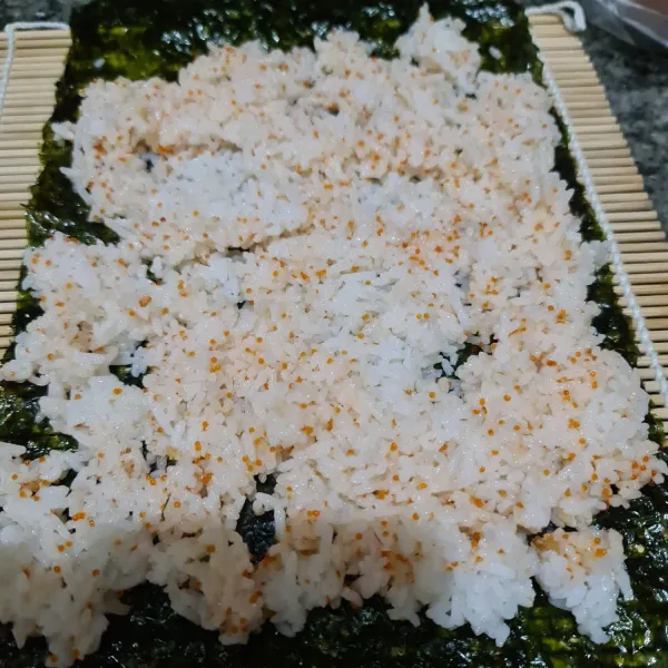 Bentangkan 1 lembar nori di atas sushi placemat, lalu beri nasi dan ratakan.