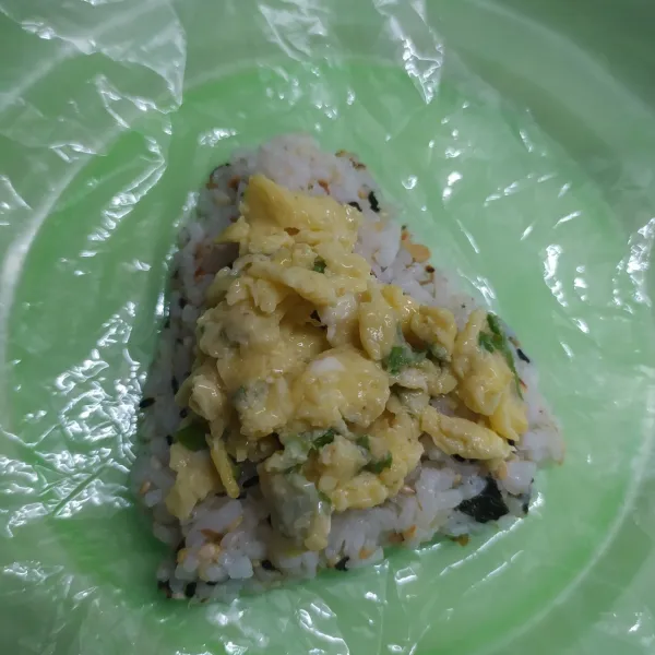 Ambil secukupnya nasi, pipihkan di atas plastik. Beri isian telur mayonaise, tutup lagi dengan nasi. Bentuk nasi kepal seperti segitiga. Bungkus lembaran nori di bagian bawah nasi. Sajikan.