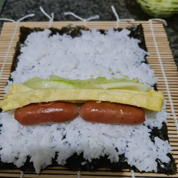 Letakkan nori sheet di atas sushi placemat, beri nasi dan ratakan. Beri sosis, telur dadar dan zucchini.