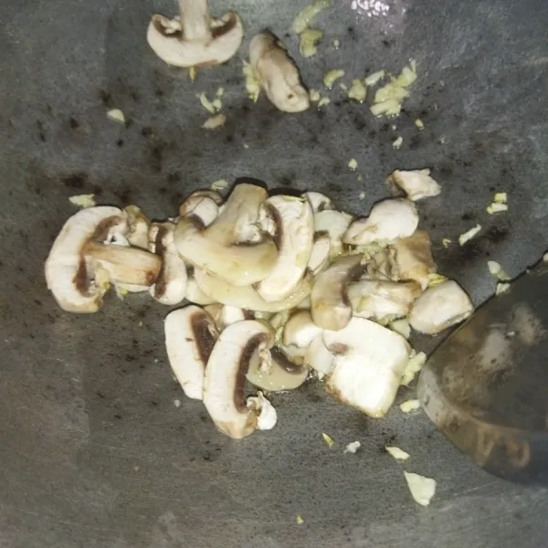 Tumis bawang putih hingga harum, masukkan potongan jamur kancing, aduk rata, masak hingga jamur layu.