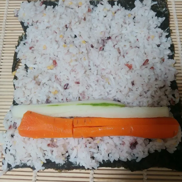 Siapkan alas sushi, tambahkan 1 lembar nori dan tata sayuran wortel dan timun.