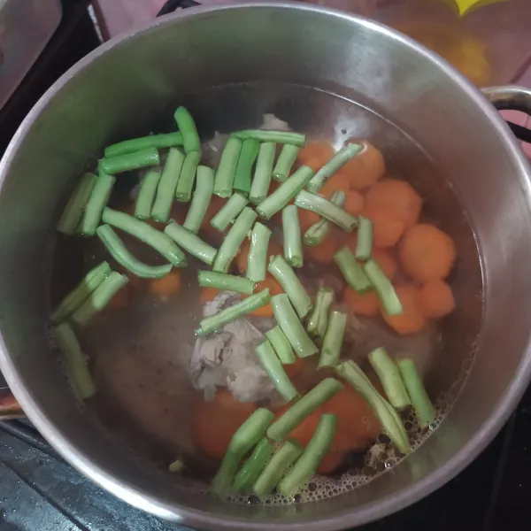 Masukkan wortel dan buncis ke dalam panci berisi air rebusan tulang yang sudah mendidih. Masak hingga setengah empuk.