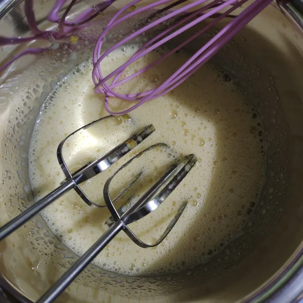 Campur bahan B telur dan gula pasir, kocok dengan whisk hingga gula larut. Bisa juga dibantu mixer pelan saja sampai larut sepenuhnya, lalu bantu whisk untuk mengambil gula dari pinggirannya. Pastikan gula larut sampai kocokannya seperti ini, putih agak encer tapi telurnya tidak mengembang. Supaya cepat larut, saat melelehkan cokelat blok bisa sambil mencampur telur dan gula dahulu di wadah adonan agar gulanya larut.