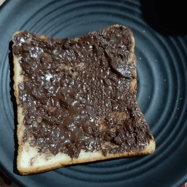 Ambil selembar roti tawar lalu plesi dengan selai cokelat.