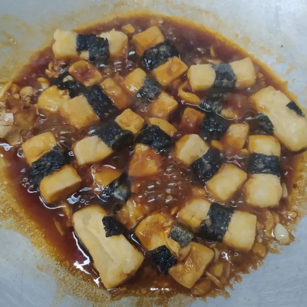 Masukkan tahu nori goreng. Masak sebentar sampai tercampur saus. Angkat dan sajikan dengan taburan wijen sangrai dan irisan daun bawang.