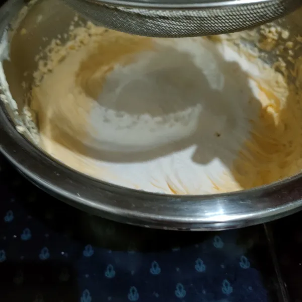 Masukkan tepung terigu, susu bubuk, dan baking powder ke dalam adonan kuning telur sembari di ayak, lalu aduk hingga rata tapi tidak over mix.