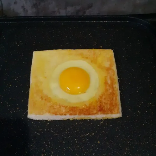 Nyalakan kompor dengan api kecil. Panggang satu sisi roti, kemudian balikkan. Ceplok telur di bagian tengahnya.