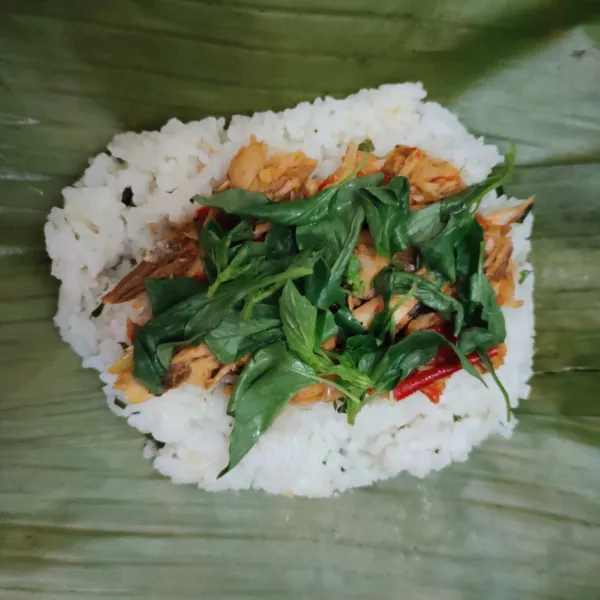 Bungkus nasi, cakalang, dan beri daun kemangi menggunakan daun pisang yang sudah di bakar.