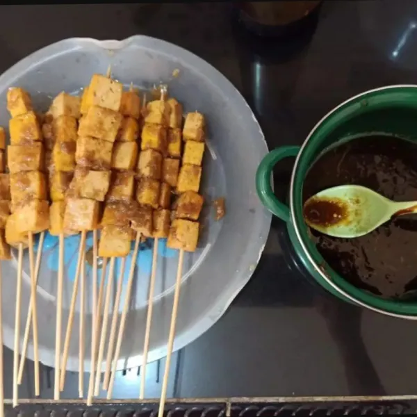 Cuci dan keringkan tusuk sate. Tusuk beberapa potong tahu (sy 5 potong). Siapkan bumbu oles : tambahkan kecap dan minyak sayur pada sisa bumbu tahu.aduk rata.