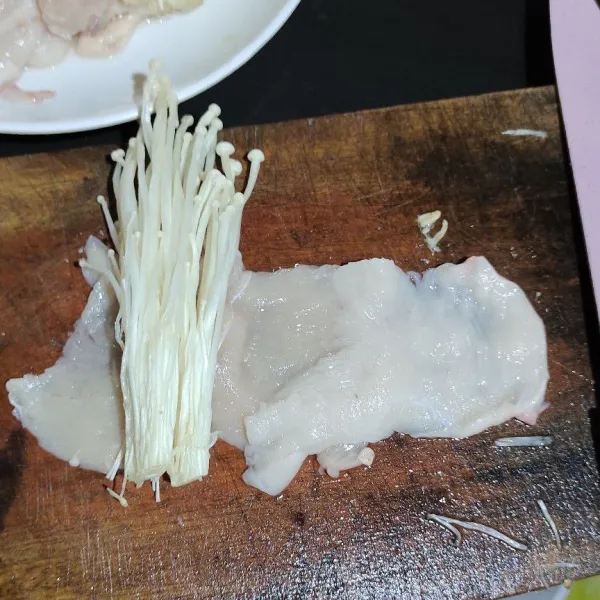 Tumpuk 2 bagian daging ayam ke samping agar bisa melilit jamur enoki lalu gulung.