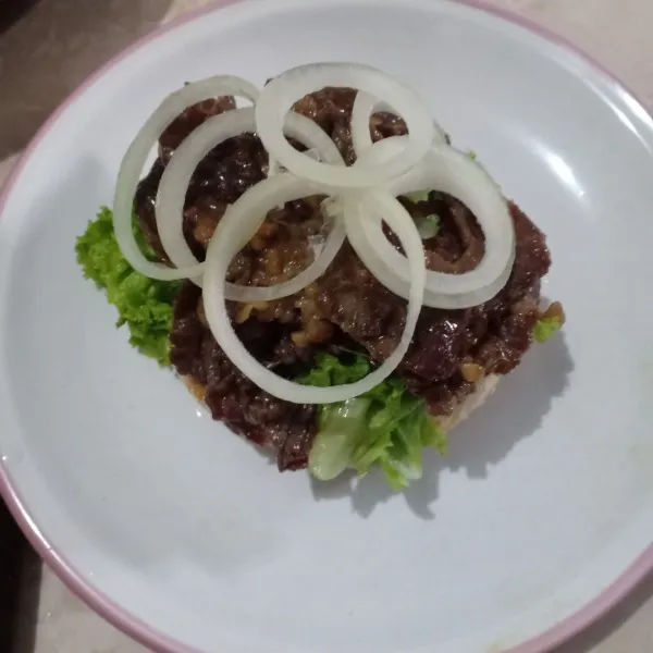 Tambahkan irisan bawang bombay, lalu tutup burger dan sajikan.