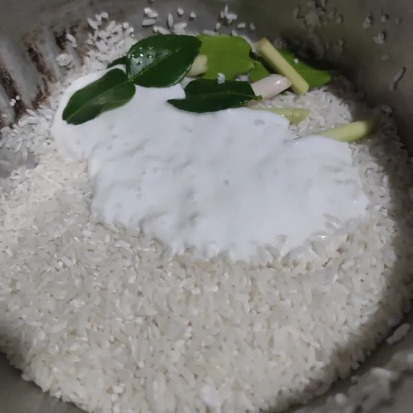 Masukkan serai, daun jeruk dan santan instan ke dalam wadah beras yang sudah dicuci.