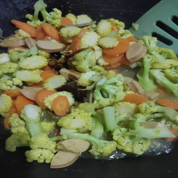 Masukkan wortel dan jagung yang sudah di cuci, lalu aduk rata. Tambahkan saus tiram, minyak wijen, gula pasir, dan garam, lalu aduk rata. Masak hingga sayur sedikit layu, lalu cicipi rasanya.