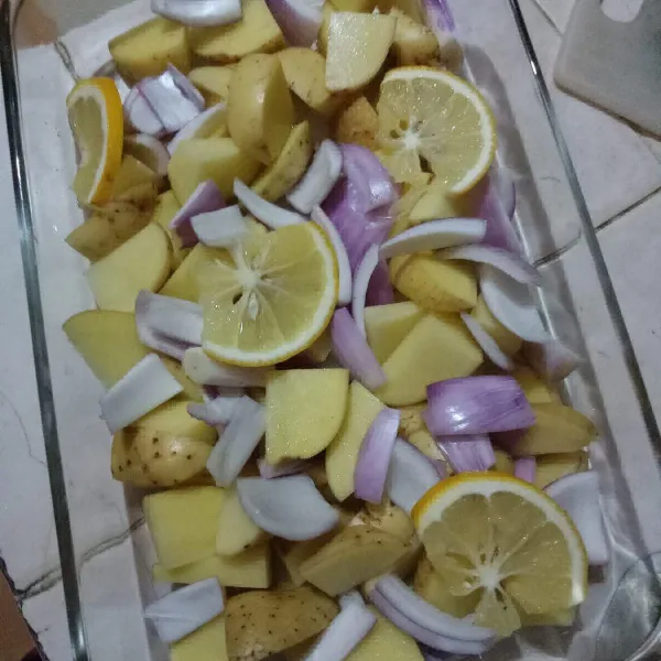 Siapkqn kentang kulit yang sudah dipotong, bawang bombay, dan lemon iris, tata di wadah tahan panas.