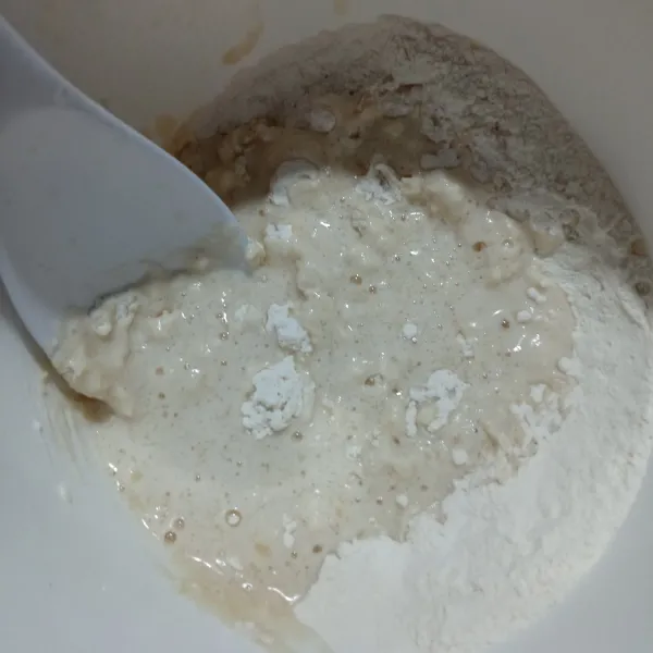 Siapkan tepung di dalam wadah, lalu masukkan campuran ragi, gula, garam dan minyak. Aduk hingga tercampur rata.