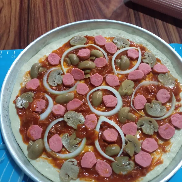 Oleskan saus bolognese secukupnya di atas adonan pizza, lalu tata topping di atasnya.