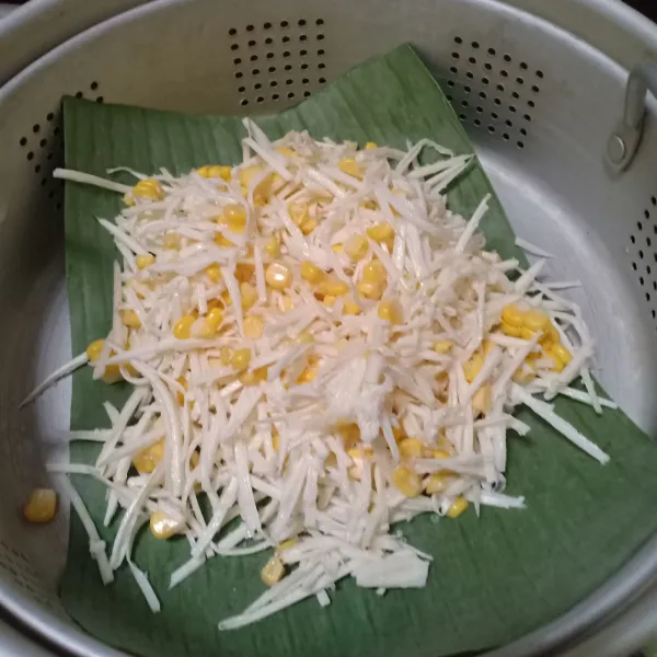 Alasi kukusan dengan daun pisang, kukus singkong dan jagung tadi selama 15 menit. Angkat dan sajikan bersama taburan kelapa.