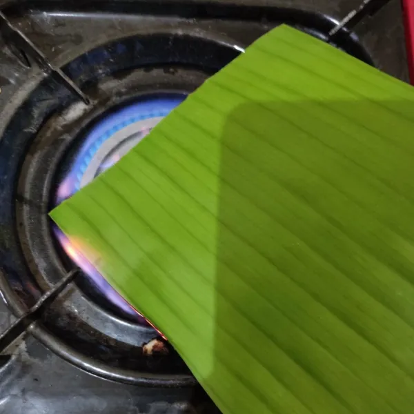 Lemaskan daun pisang dengan dibakar dengan api kecil agar layu dan tidak patah saat dibuat membungkus.