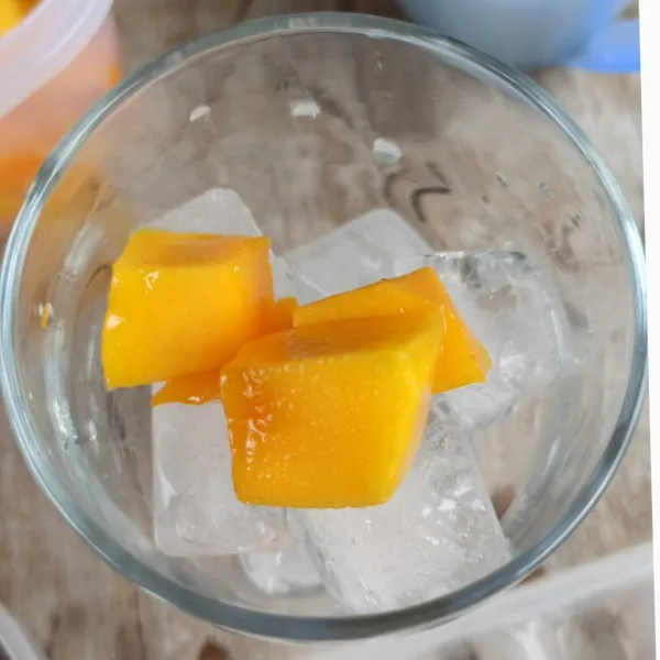 Untuk penyajian, masukkan es batu ke gelas, beri buah mangga.