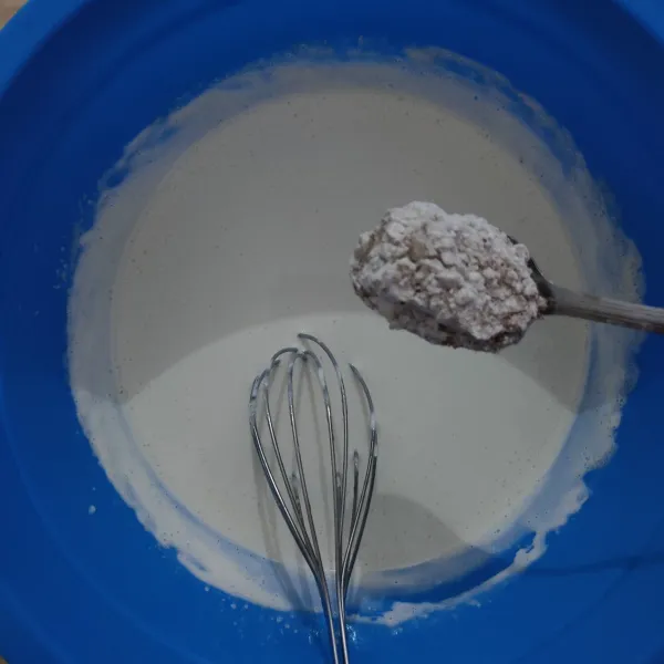 Masukkan campuran tepung sedikit demi sedikit, sambil terus diaduk menggunakan whisker hingga tercampur rata.