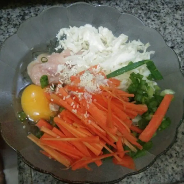 Dalam wadah, campur telur, daging ayam giling, garam, kaldu jamur, merica bubuk, bawang putih, bawang bombay, wortel, kol dan bawang daun, aduk rata