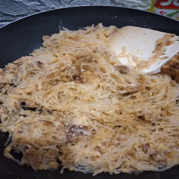 Besarkan api, tambahkan kaldu penyedap dan lada bubuk. Masak hingga air menyusut dan bihun kering.