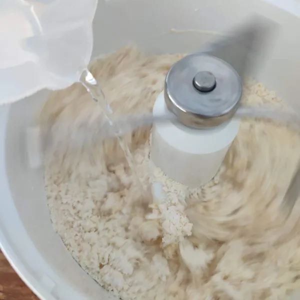 Nyalakan mixer/ uleni sambil tuangkan air sedikit demi sedikit sampai membentuk adonan ½ kalis.