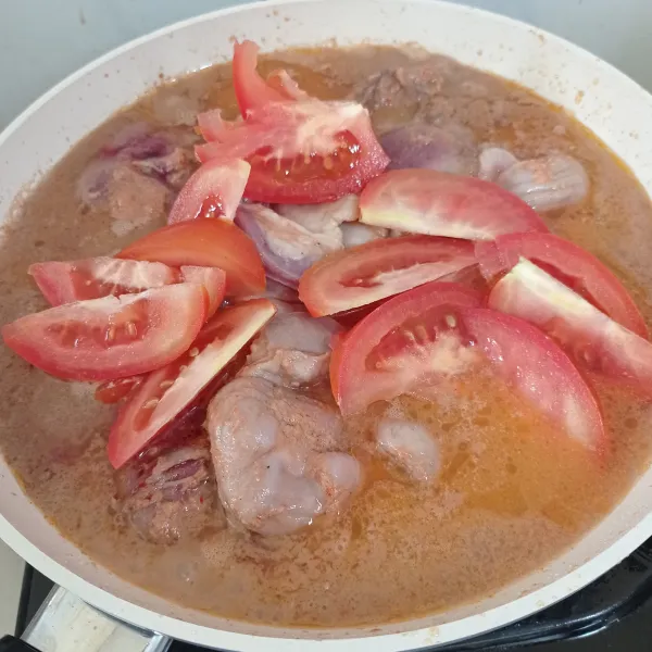 Masak daging dan bumbu hingga setengah mengering. Tambahkan air dan tomat.