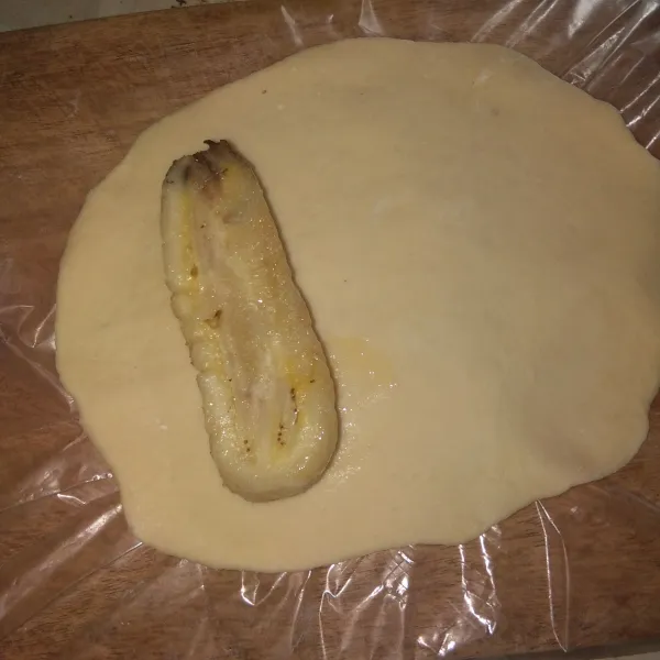 Gilas adonan lalu beri isian pisang, lalu gulung.