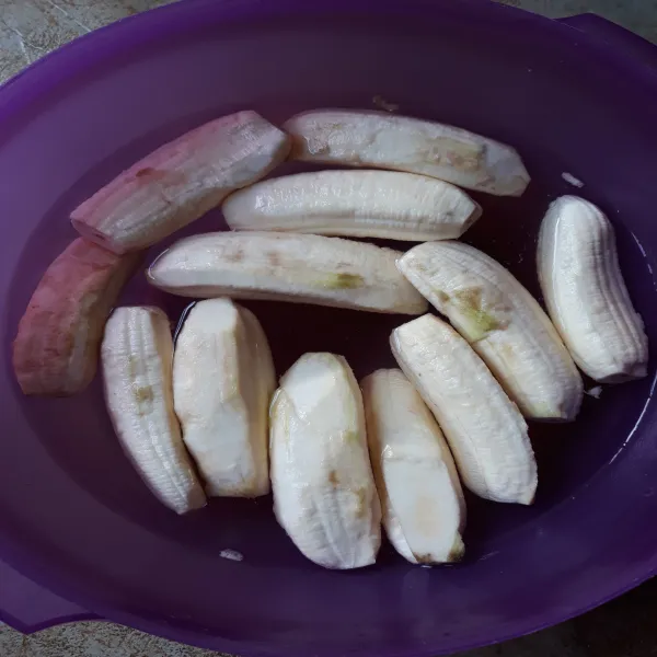 Siapkan baskom berisi air. Kupas kulit pisang lalu langsung masukkan pisang yang dikupas dalam air.