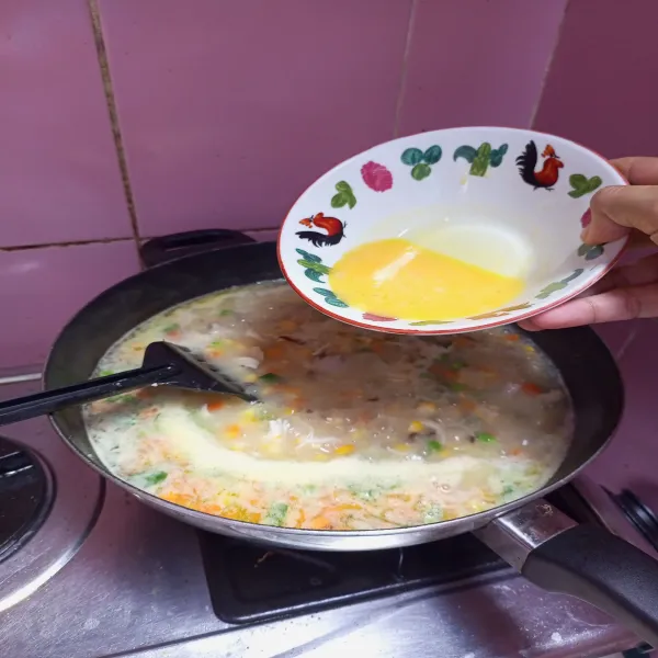Masukkan kocokan telur sedikit-sedikit ke dalam rebusan sup sambil diaduk sampai berserabut.