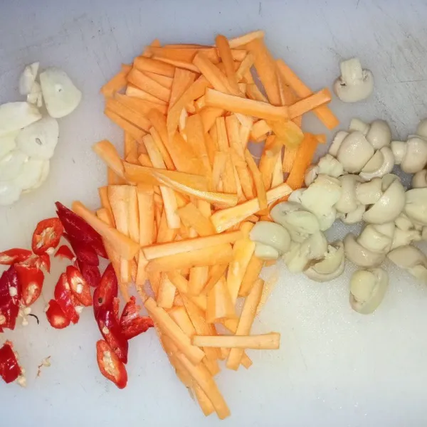 Potong korek wortel dan untuk jamur potong menjadi dua bagian jamur kancing. Rajang bawang putih dan cabai merah.
