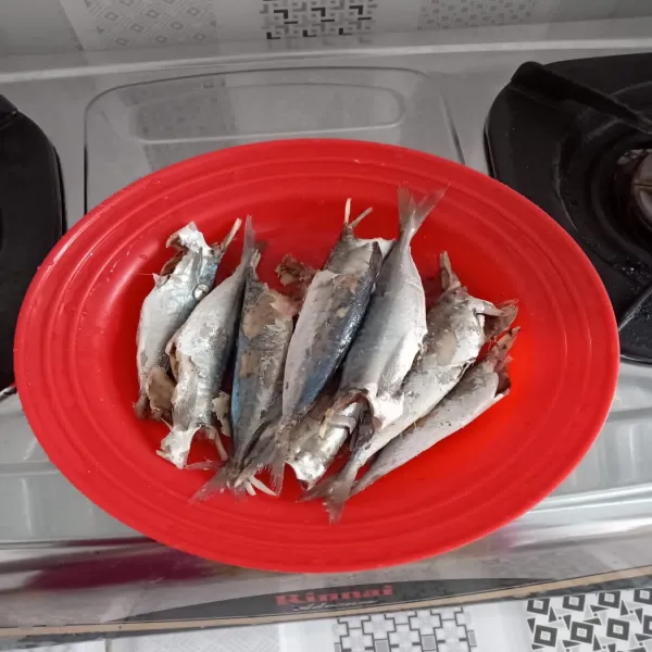 Bersihkan ikan pindang, buang isi perut dan kepala. Siram ikan dengan air bersih.