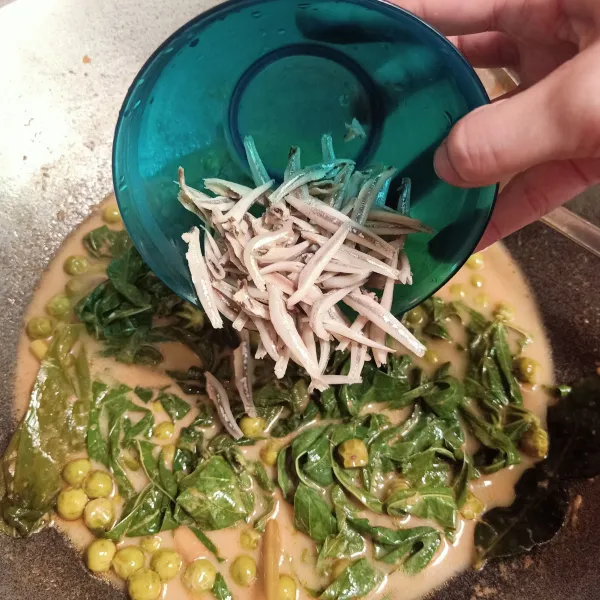 Kemudian masukan daun singkong dan ikan teri yang sudah dicuci terlebih dahulu, aduk rata.